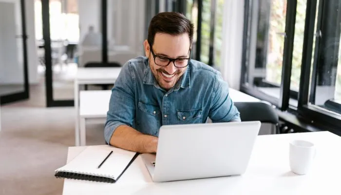 A smiling man sitting behind a desk working on his laptop