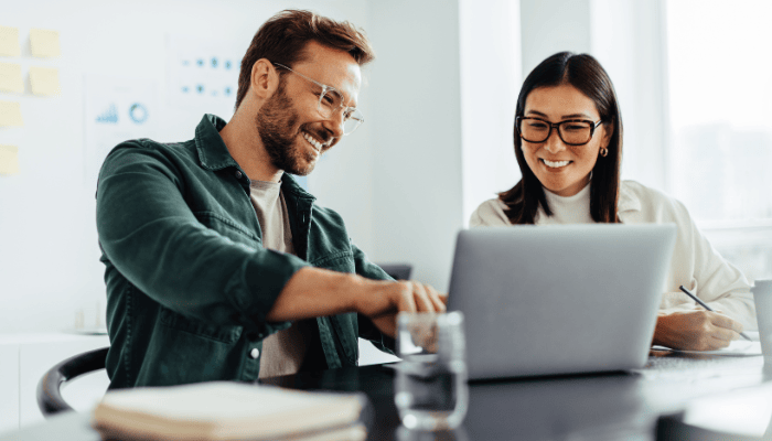 Two business people using a laptop together while sitting in a meeting. Happy business people reading myths about SaaS partner programs