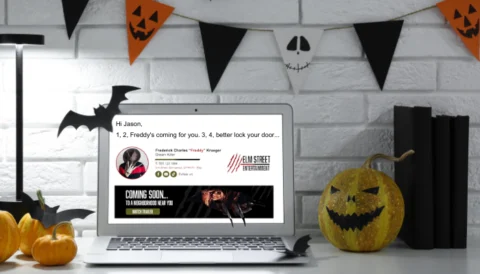 A laptop featuring a Halloween-themed email signature of Freddy Krueger, complete with a spooky banner, set in a Halloween-decorated office.