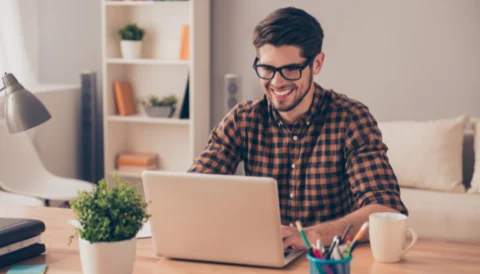 Cheerful young man in glasses typing on laptop in a casual setting