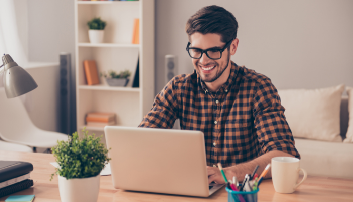 Cheerful young man in glasses typing on laptop in a casual setting