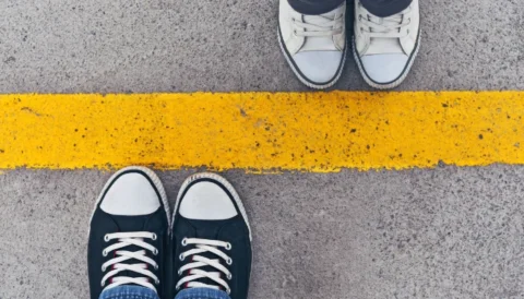 Top view of two pairs of sneakers standing on opposite sides of a yellow dividing line