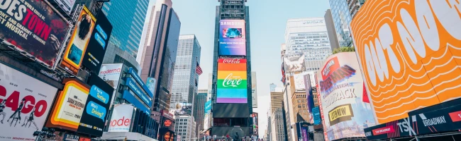 A buy time square with people walking in the street and and billboards are lighting the scene